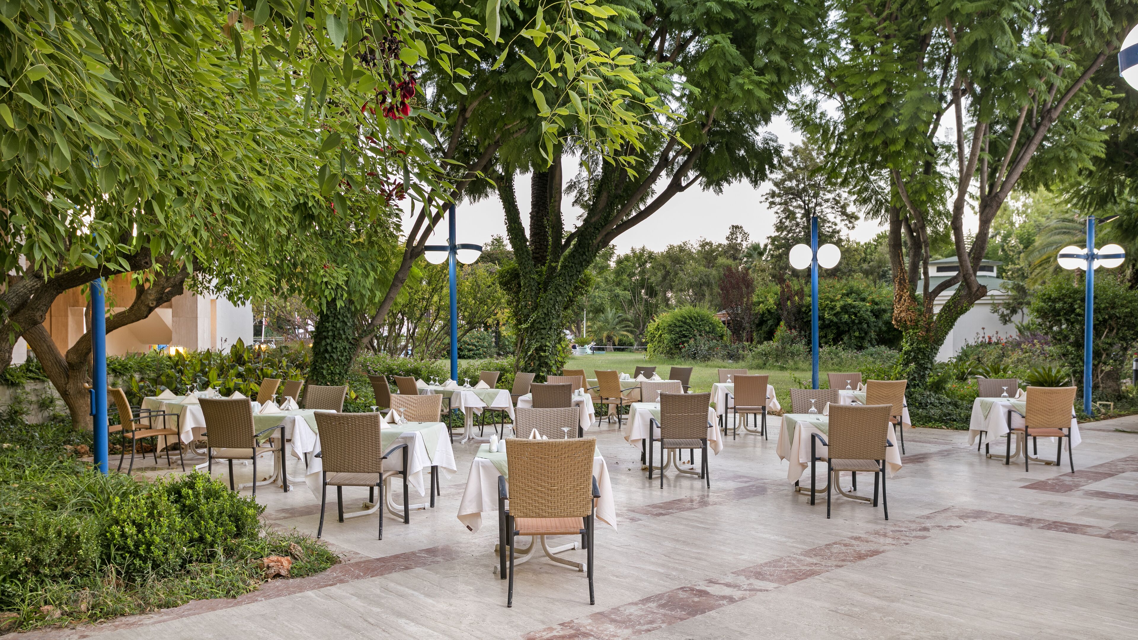 An outdoor dining area with tables and chairs arranged under trees.