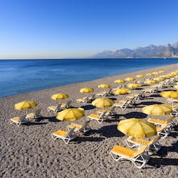 Relax on the beach with comfortable sun loungers and umbrellas, surrounded by calm waters and majestic mountains.