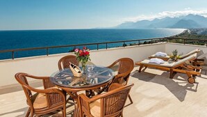 A balcony with wicker furniture, a glass table, and a view of the sea and mountains. - Özkaymak Falez Hotel (Antalya)