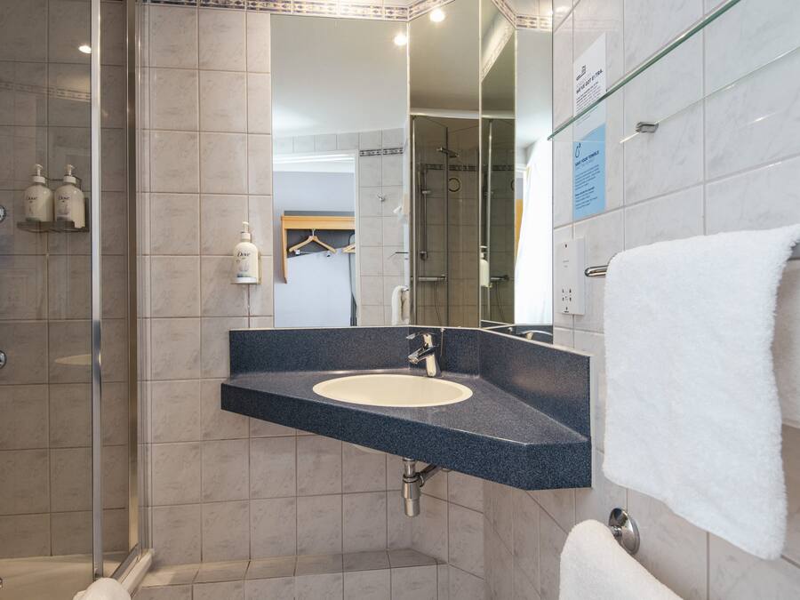 A bathroom with a glass shower enclosure, a sink with a dark countertop, and a white towel hanging on a rack.