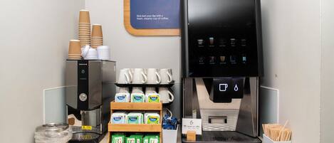 Una estación de café con una máquina de café, vasos desechables y cápsulas de café.