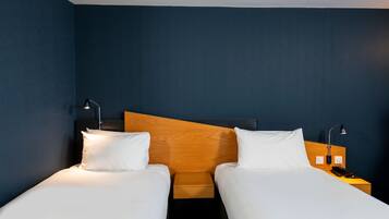 A hotel room with two single beds, wooden headboards, bedside tables with lamps, and a nightstand with a phone.