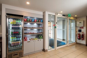 A hotel lobby with a beverage vending machine stocked with various drinks, snack shelves, and a glass door entrance. - Holiday Inn Express Stirling by IHG (Stirling)