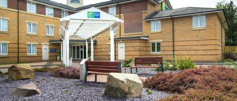 A Holiday Inn Express with a covered entrance, outdoor seating, and landscaped garden area.