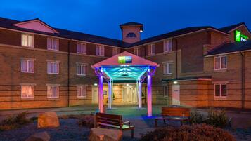 Welcome to our hotel, featuring a unique tower on the roof and a beautifully landscaped entrance with benches.