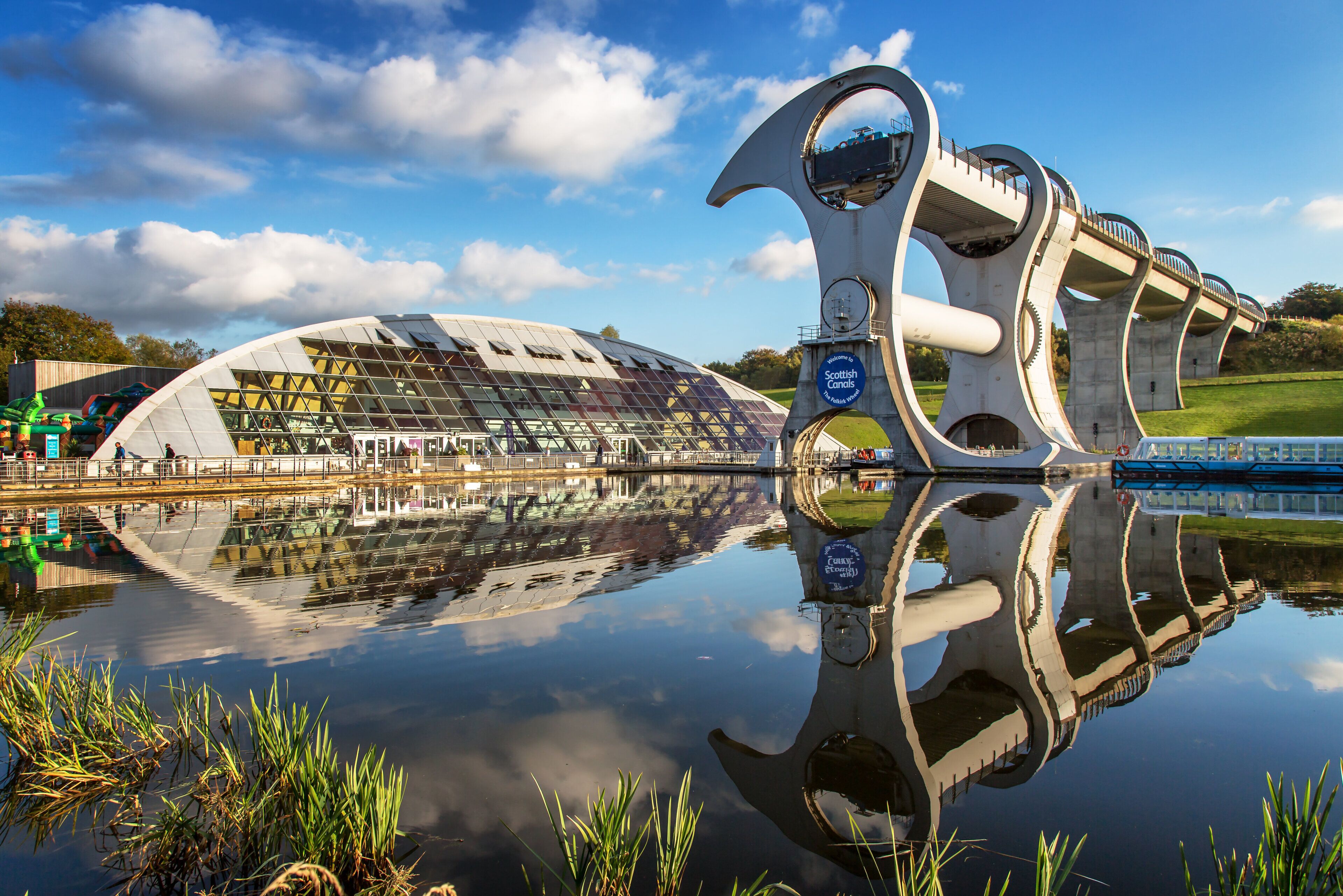 Una estructura arquitectónica moderna con fachada de vidrio y un elemento circular que se refleja en el agua.