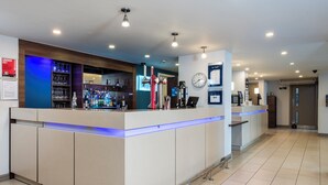 A modern hotel lobby with a reception desk, a clock on the wall, and a bar area with various bottles and glasses. - Holiday Inn Express Stirling by IHG (Stirling)