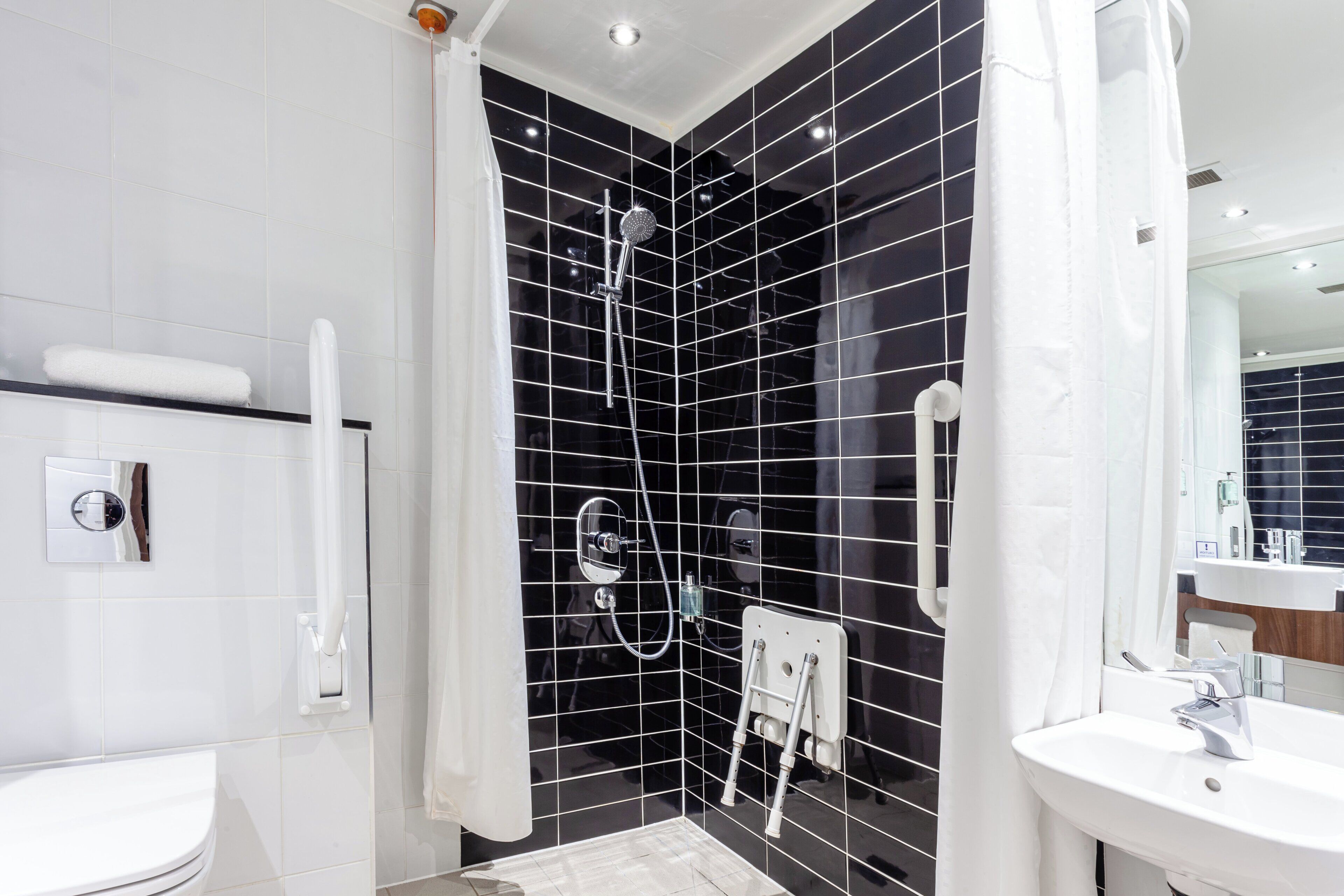 A modern bathroom with a black tiled shower, a white sink, and a mirror.