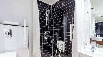 A modern bathroom with a black tiled shower, a white sink, and a mirror.