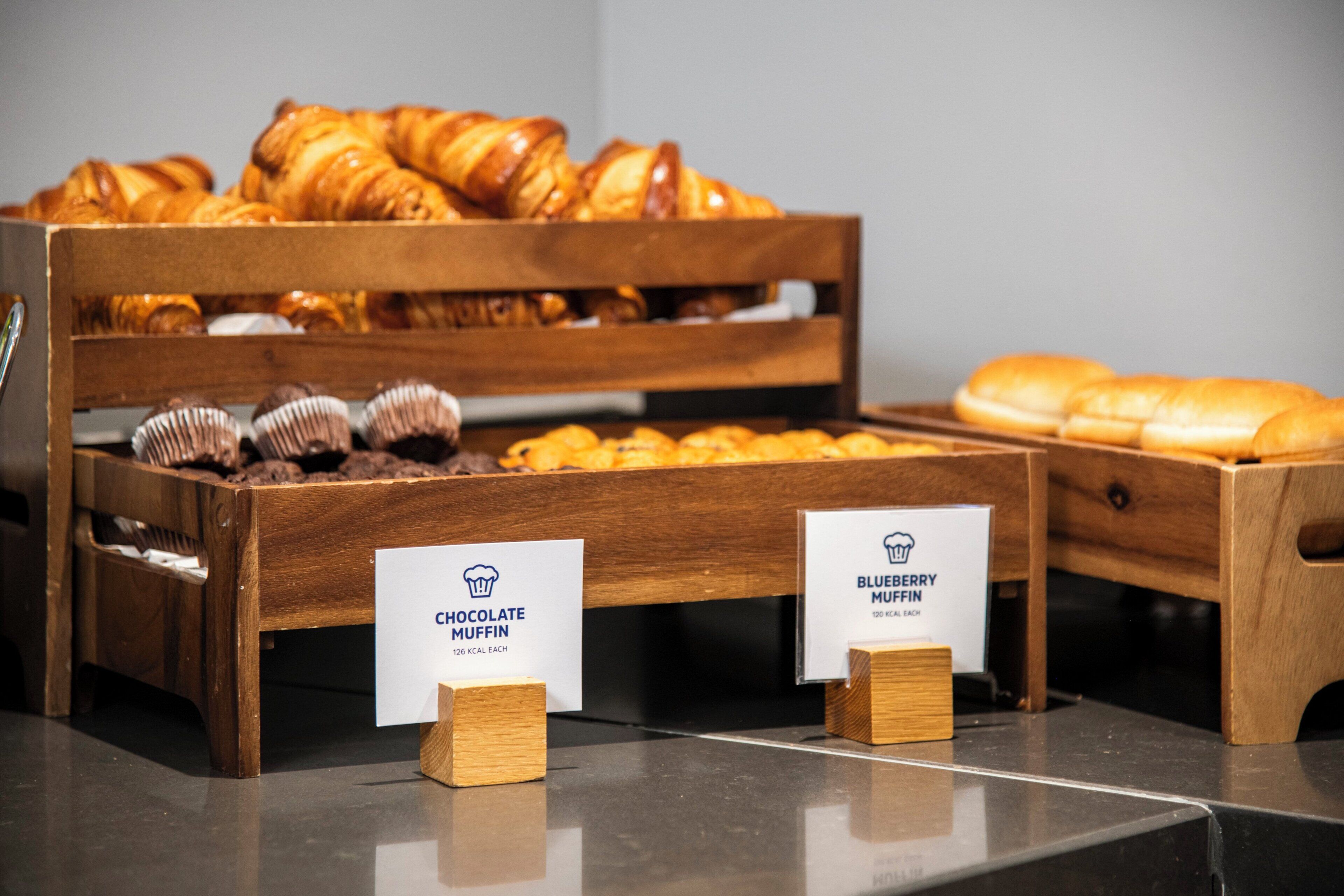 Exposição de produtos de panificação, incluindo muffins de chocolate e muffins de blueberry.