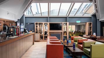 A modern hotel lobby with a bar area, seating, and a large TV screen.