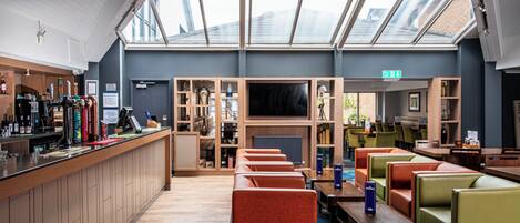 A modern hotel lobby with a bar area, seating, and a large TV screen.