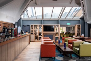 A modern hotel lobby with a bar area, seating, and a large TV screen. - Holiday Inn Express Edinburgh Airport by IHG (Newbridge)
