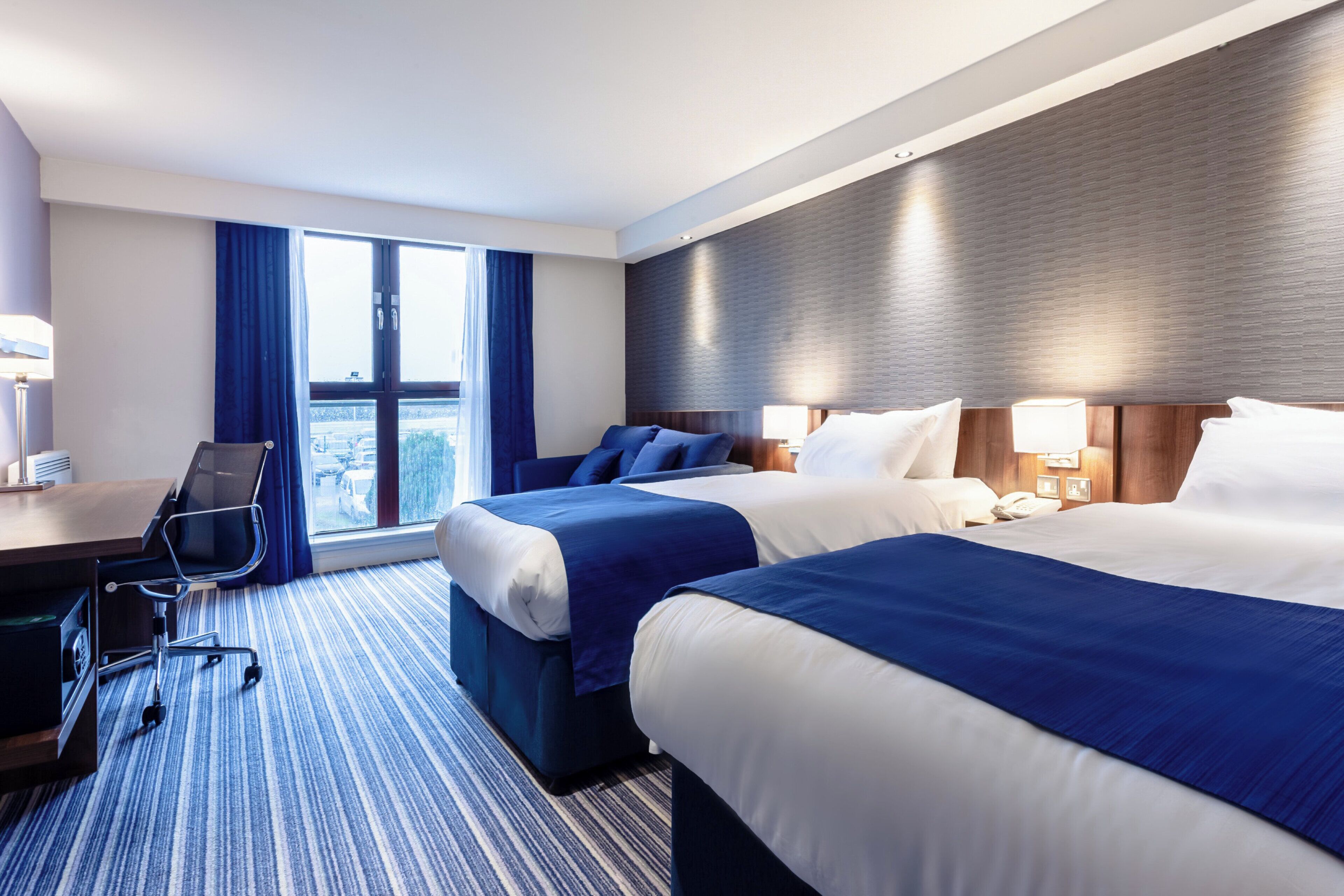 A hotel room with two beds, a desk, and a chair.