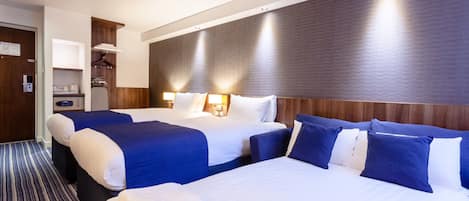 A hotel room with two beds, a wooden headboard, a small desk with a lamp, and a striped carpet.