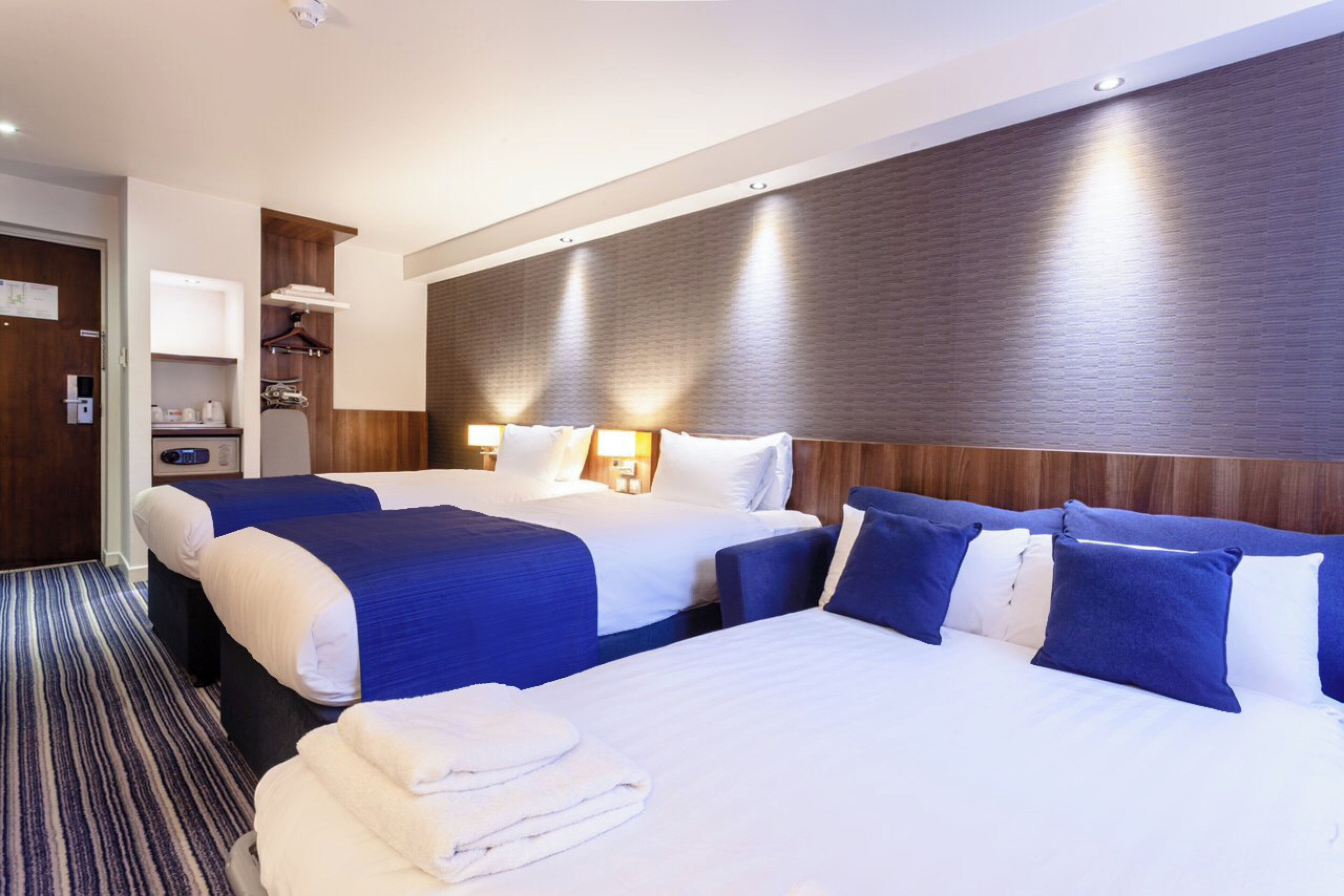 Ein Hotelzimmer mit zwei Betten, einem Holzkopfteil, einer kleinen Sitzecke und einer Tür.