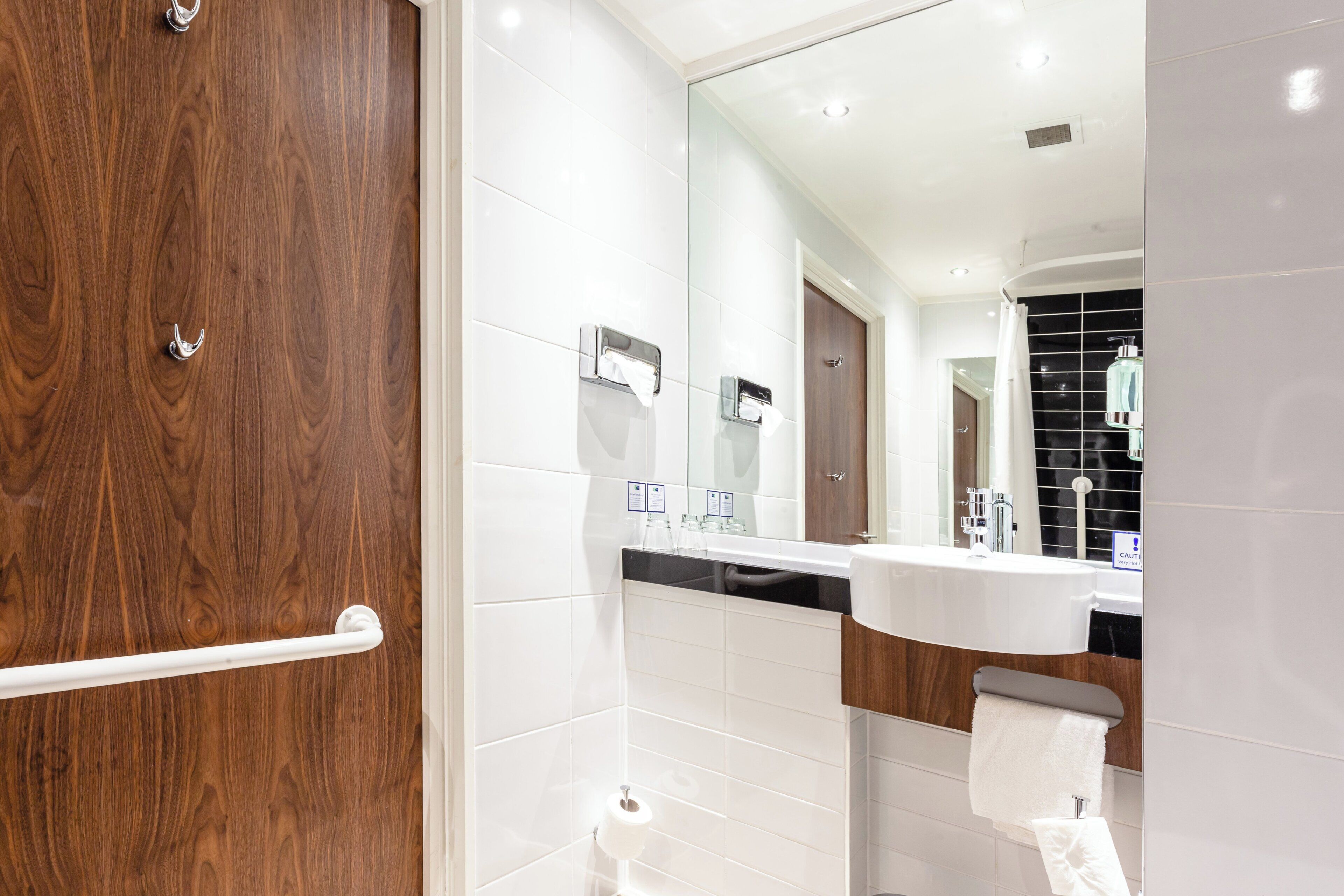 Un baño moderno con puerta de madera, azulejos blancos, encimera negra y espejo.