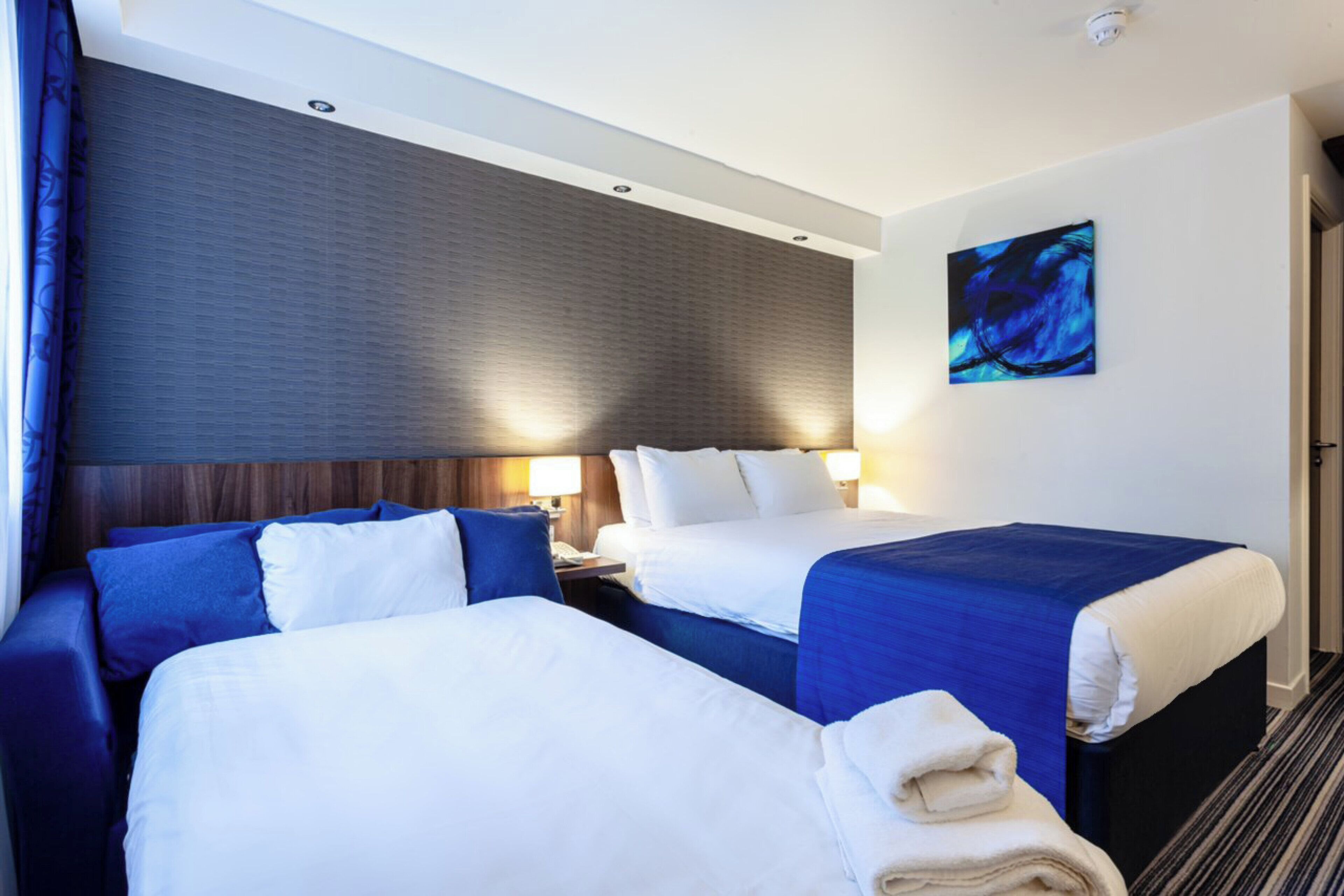 A hotel room with two beds, a large painting, and a nightstand with a lamp.