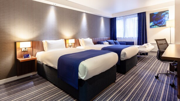A hotel room with two beds, a desk, and a chair. There is a nightstand with a lamp and a sign. - Holiday Inn Express Edinburgh Airport by IHG (Newbridge)
