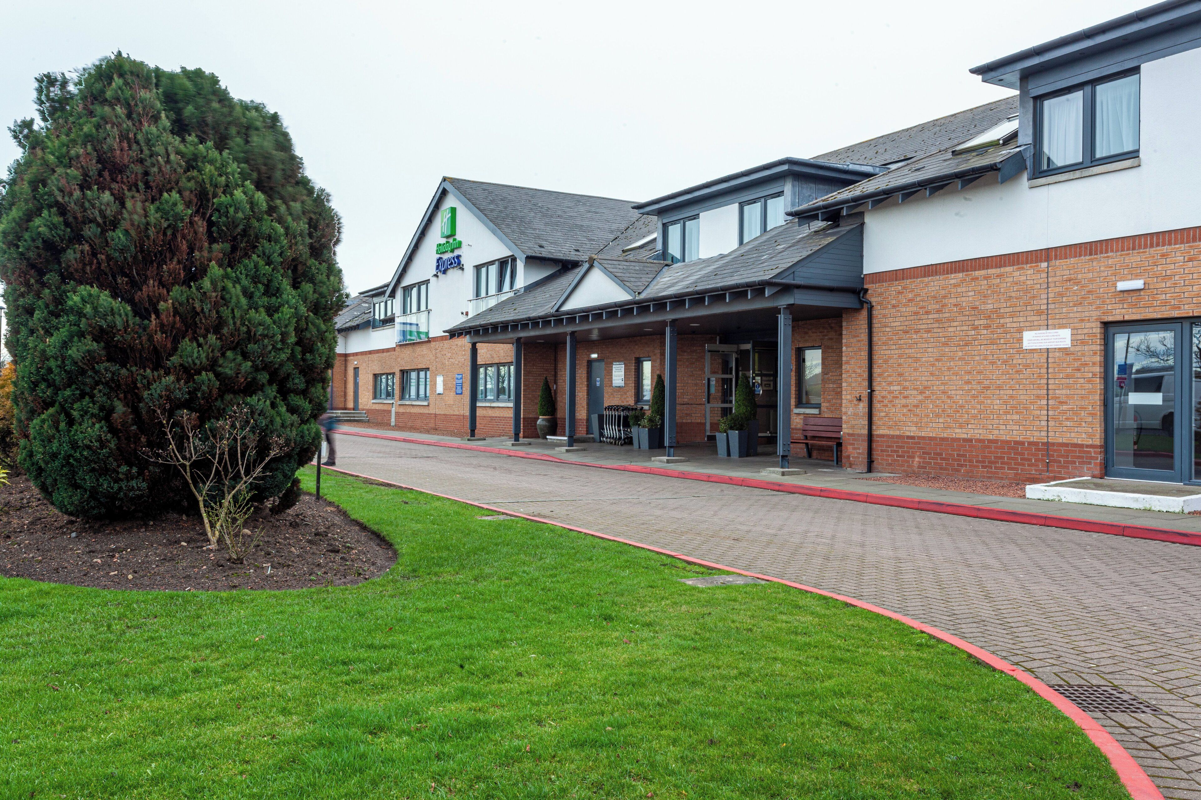 A hotel with a brick facade, a large tree in the foreground, and a covered walkway.