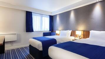 Habitación de hotel con dos camas, un escritorio y un ventanal con cortinas.
