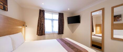 A hotel room with a large bed, a flat-screen TV mounted on the wall, and a mirror.