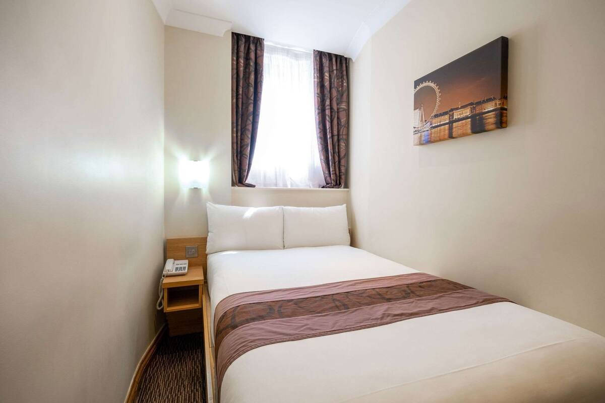 Hotellihuone, jossa on sänky, yöpöytä, jossa on puhelin, sillan kuva ja verhot.