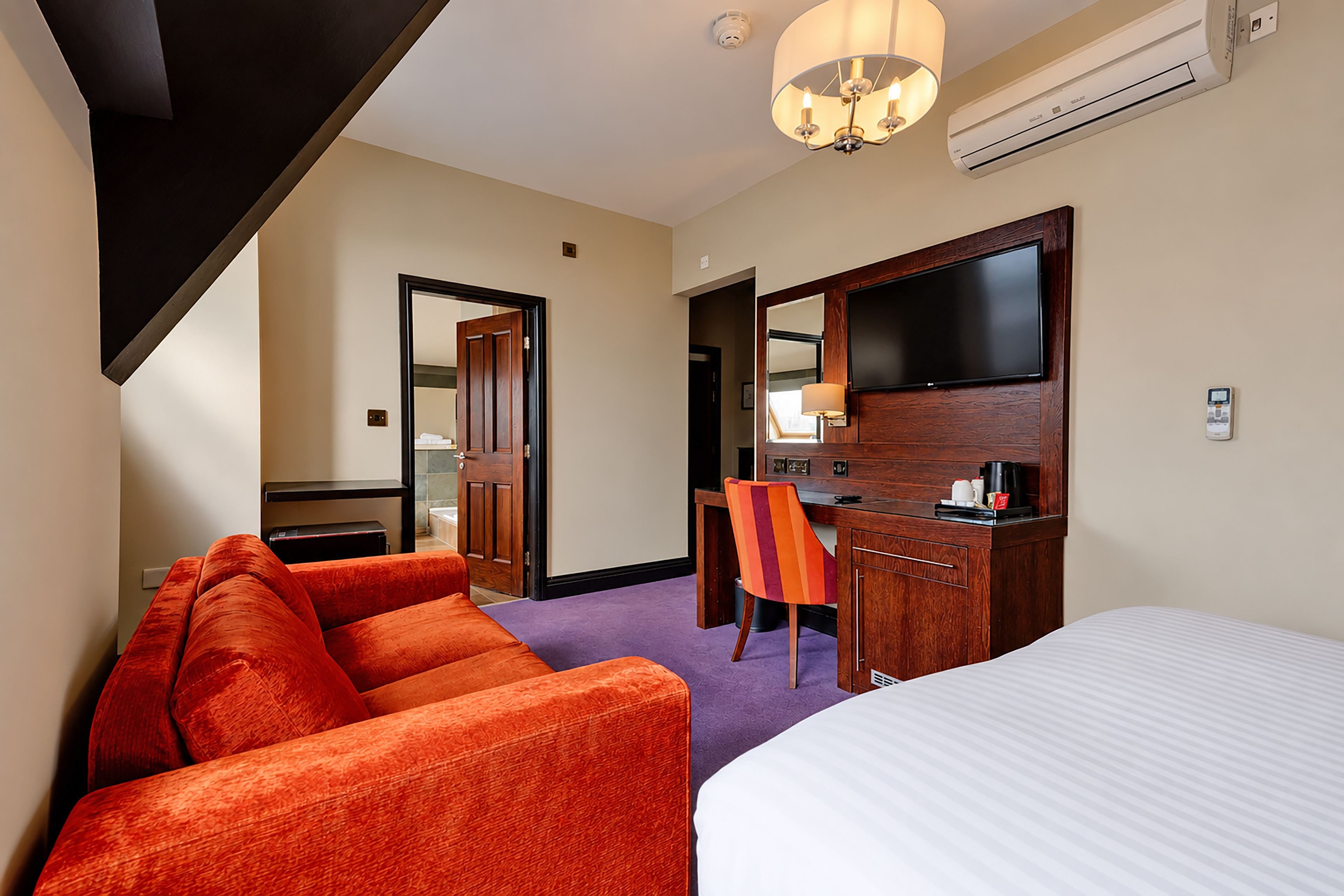 A hotel room with a bed, a desk, a chair, and a TV.