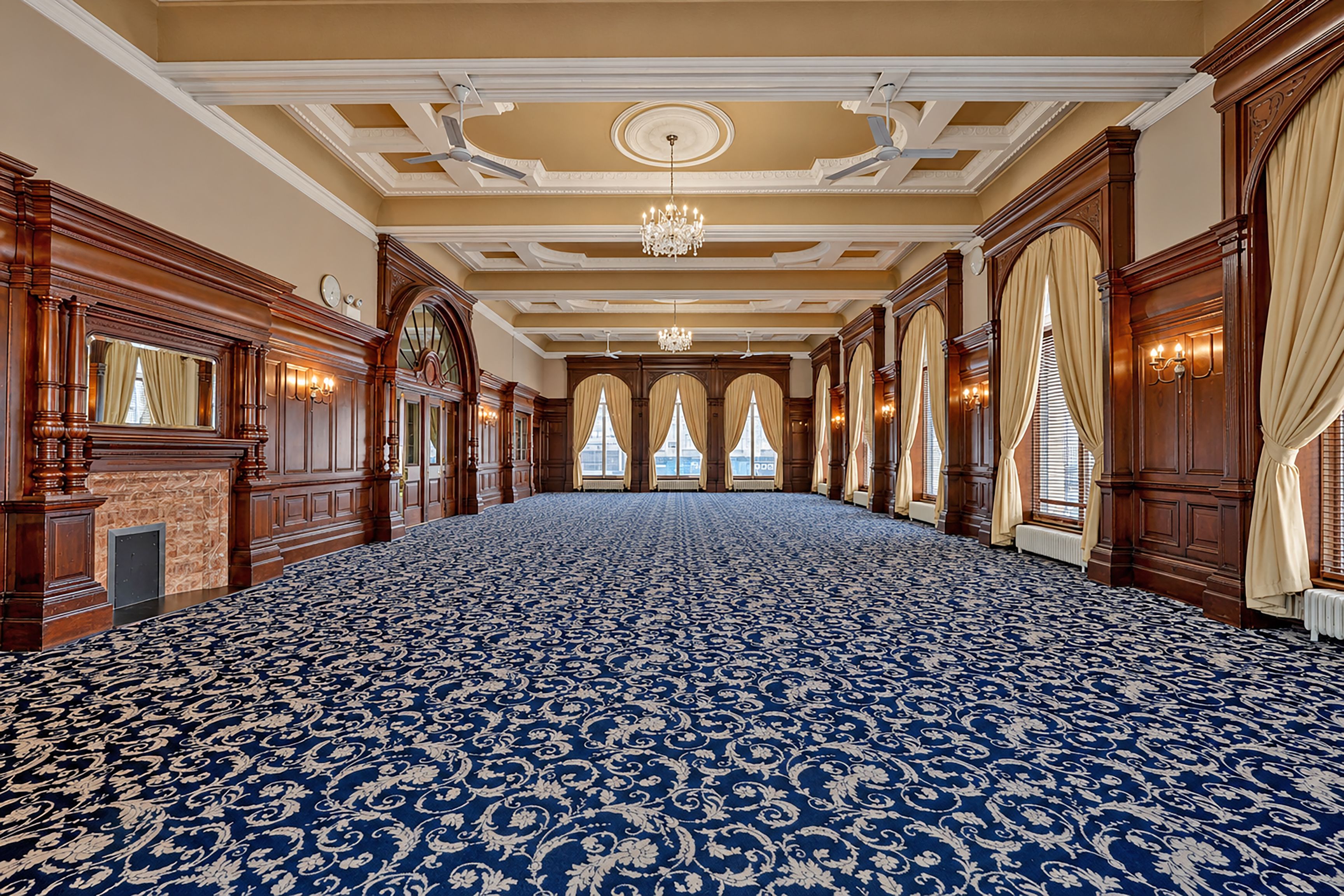 Un salón amplio y lujoso con alfombra estampada, paneles de madera y un candelabro.