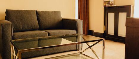 A modern living room with a glass coffee table, a grey sofa, and a dark wooden cabinet.