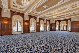 A large room with a patterned carpet, wooden paneling, and multiple windows with curtains.