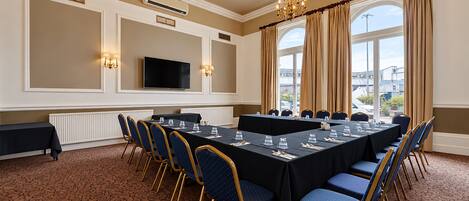 A conference room with a long table, chairs, a television, and a large window with curtains.