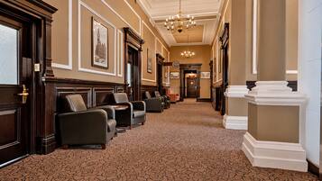 A hotel lobby with a carpeted floor, seating area with leather chairs, a chandelier, and framed pictures on the walls.