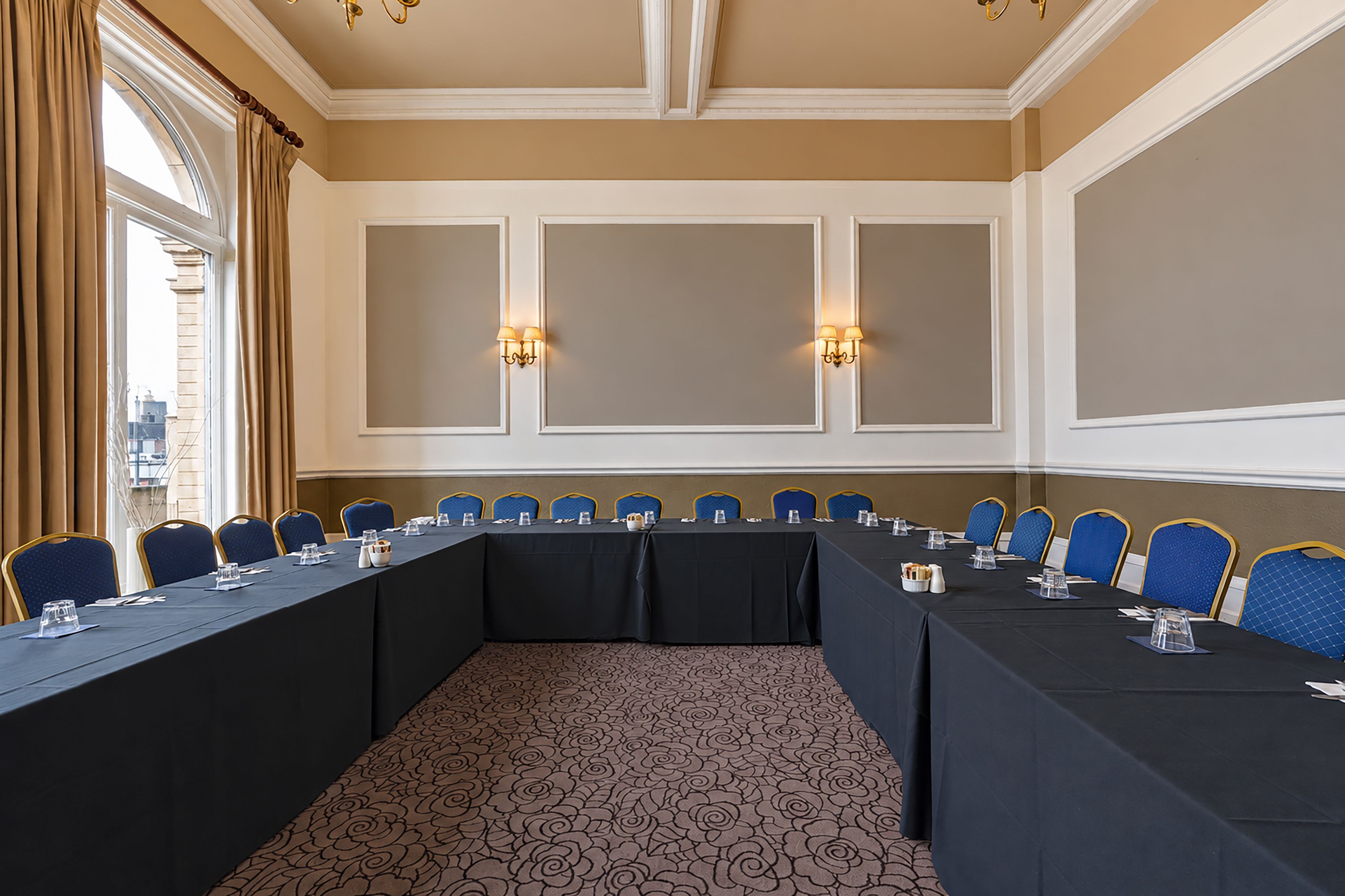 Une salle de conférence avec une longue table, des chaises bleues et des appliques murales.