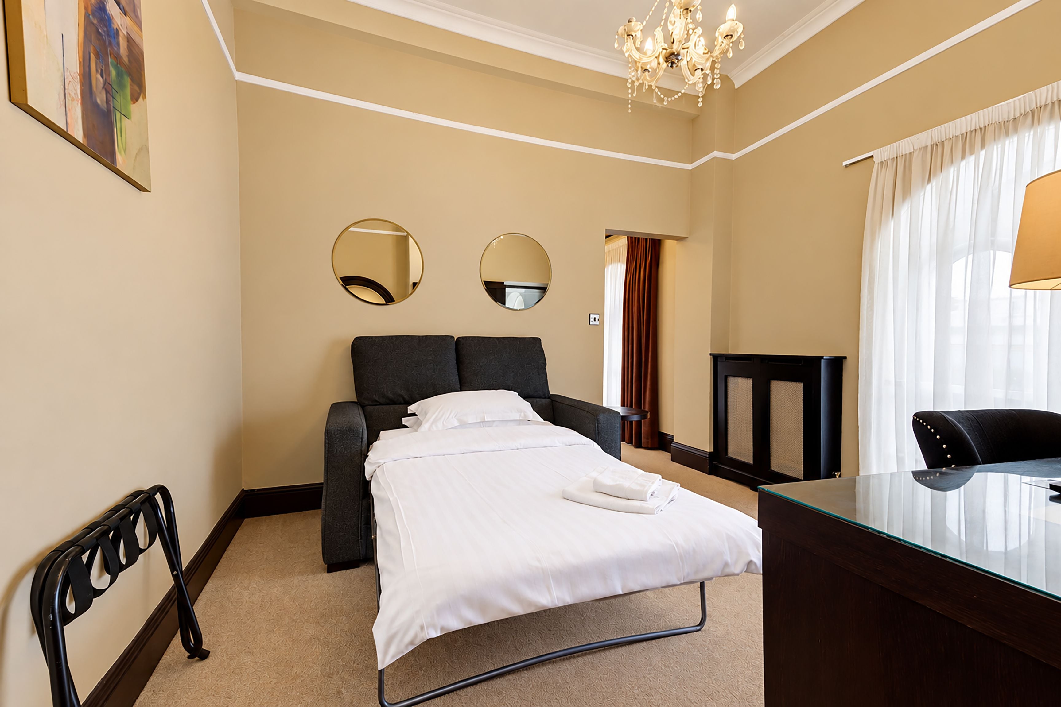 Ein Hotelzimmer mit Bett, Schreibtisch, zwei Stühlen, einem Spiegel und einer Chandelier.