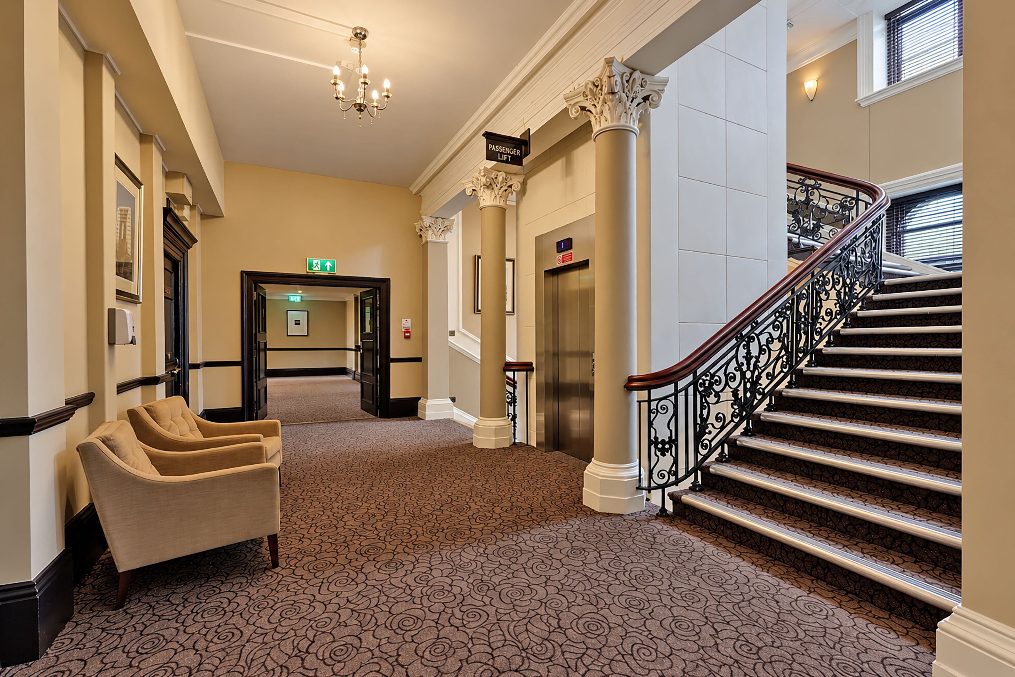 Un vestíbulo de hotel con una escalera monumental, un mostrador de recepción y un área de estar.