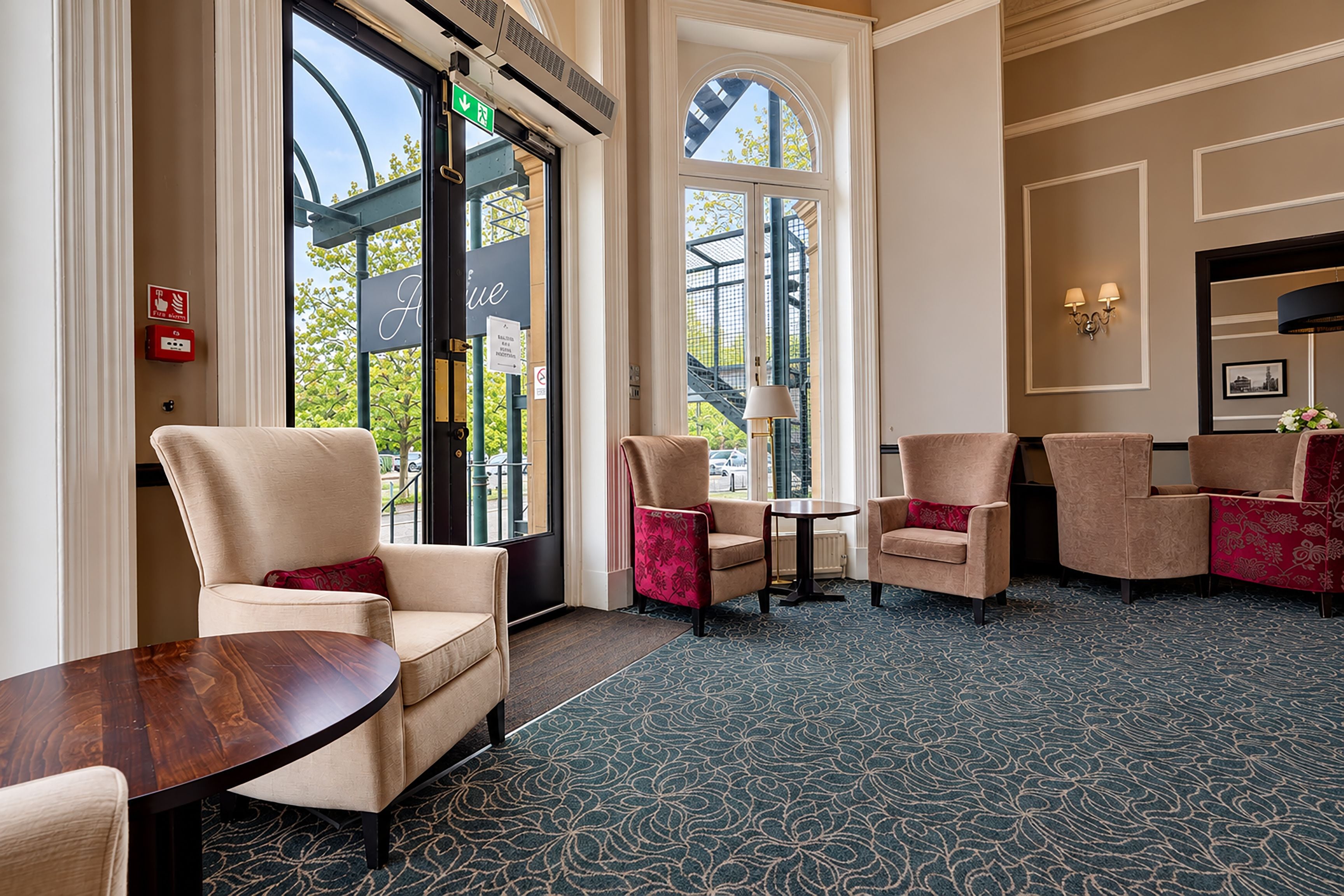 A hotel lobby with a seating area, a fire alarm, and a view of the outside.