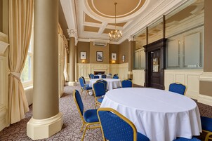 Un comedor formal con mesas redondas y sillas azules, una chimenea y un espejo grande.