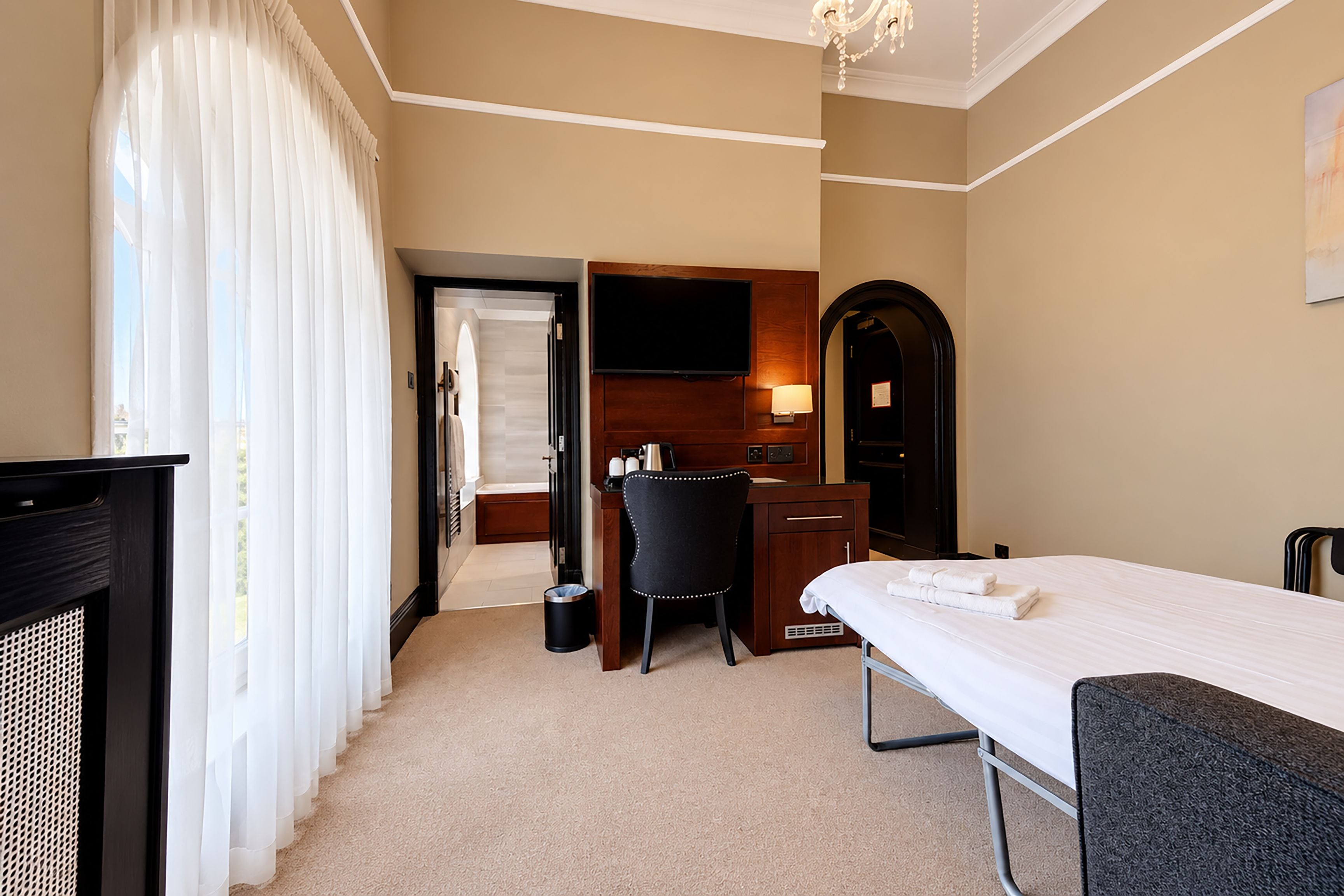 A hotel room with a bed, a desk, a chair, a television, and a bathroom visible through an open door.
