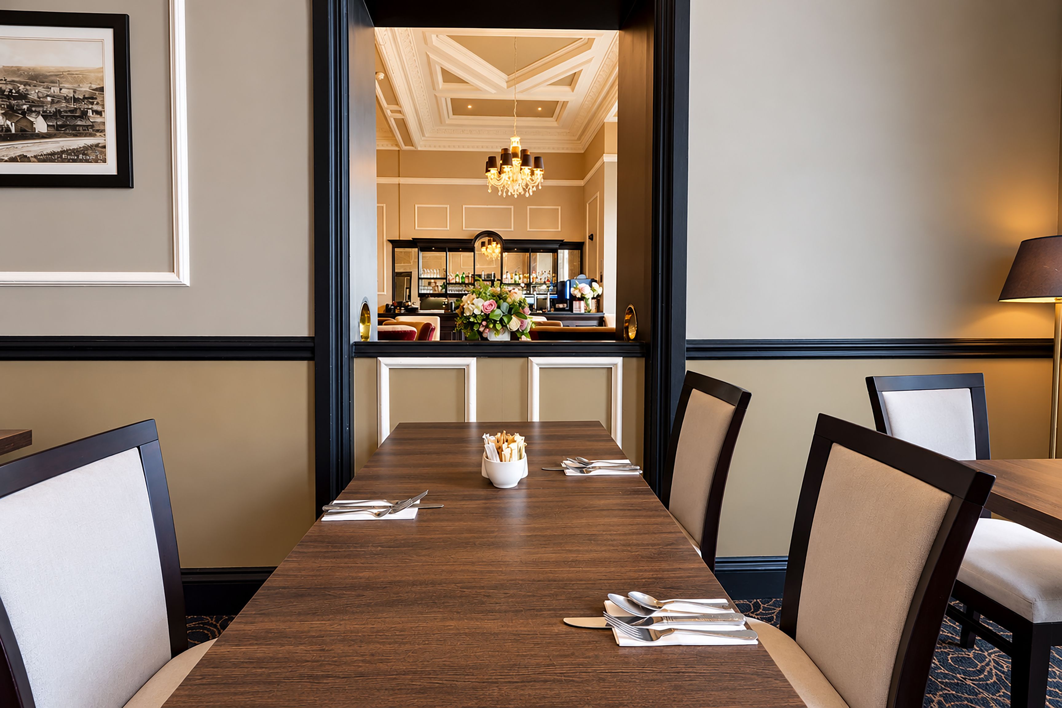 A dining area with a long wooden table, chairs, and a bar in the background.