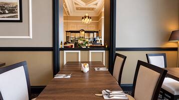 A dining area with a long wooden table, chairs, and a bar in the background.