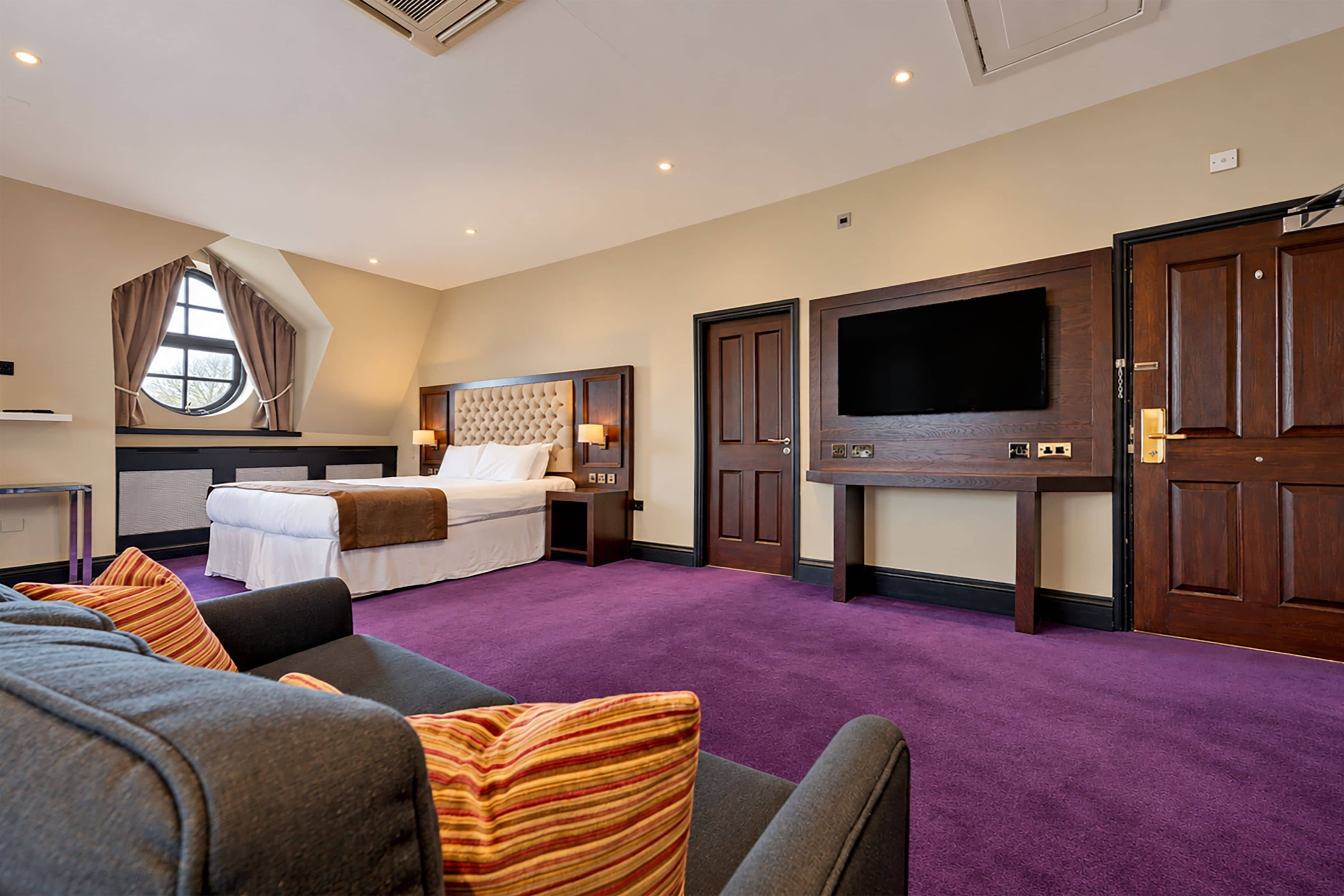 A hotel room with a bed, a TV, a sofa, and a window with curtains.