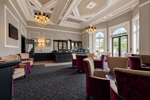 Un vestíbulo de hotel con área de bar, asientos y alfombra estampada.