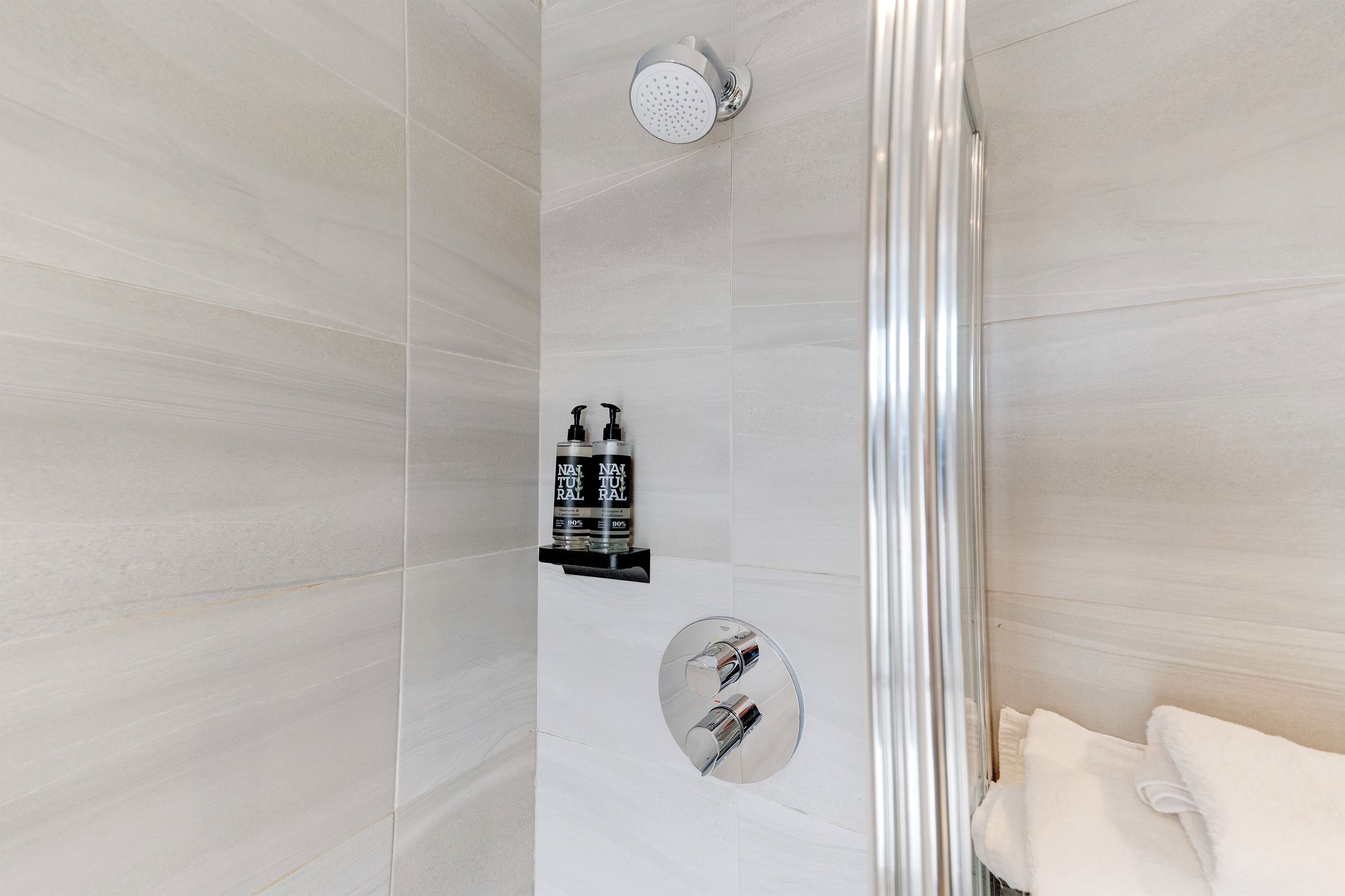 Une salle de bain moderne équipée d’une douche, d’un porte-serviettes et de deux bouteilles de shampoing.