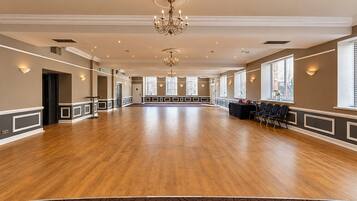 Ein geräumiger Saal mit Holzboden, einer Kristallleuchter und einer Reihe von Stühlen entlang der Wand.
