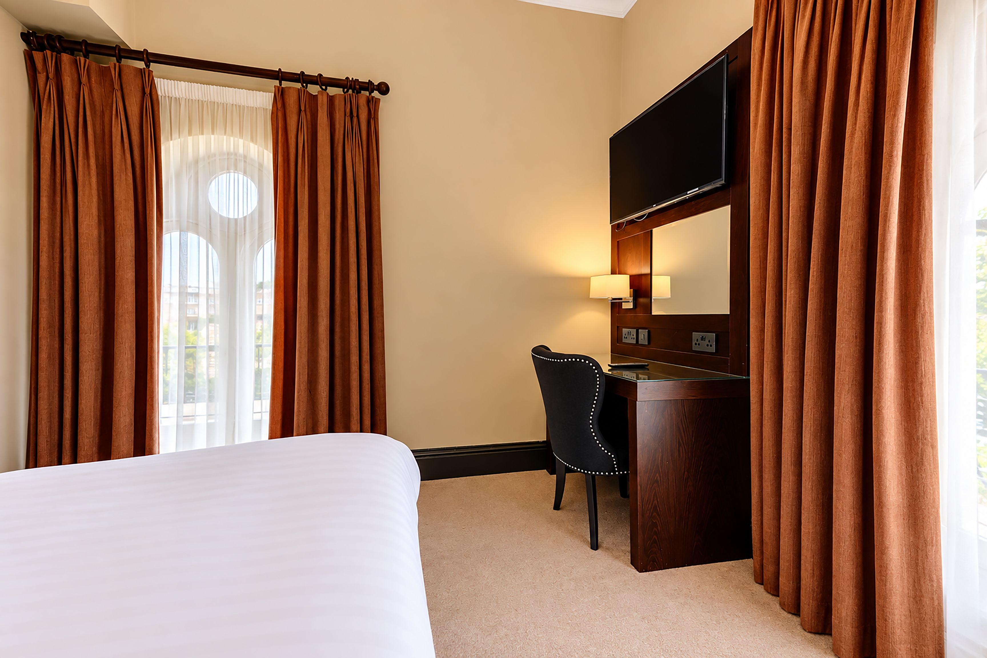 A hotel room with a bed, a desk, a chair, and curtains.
