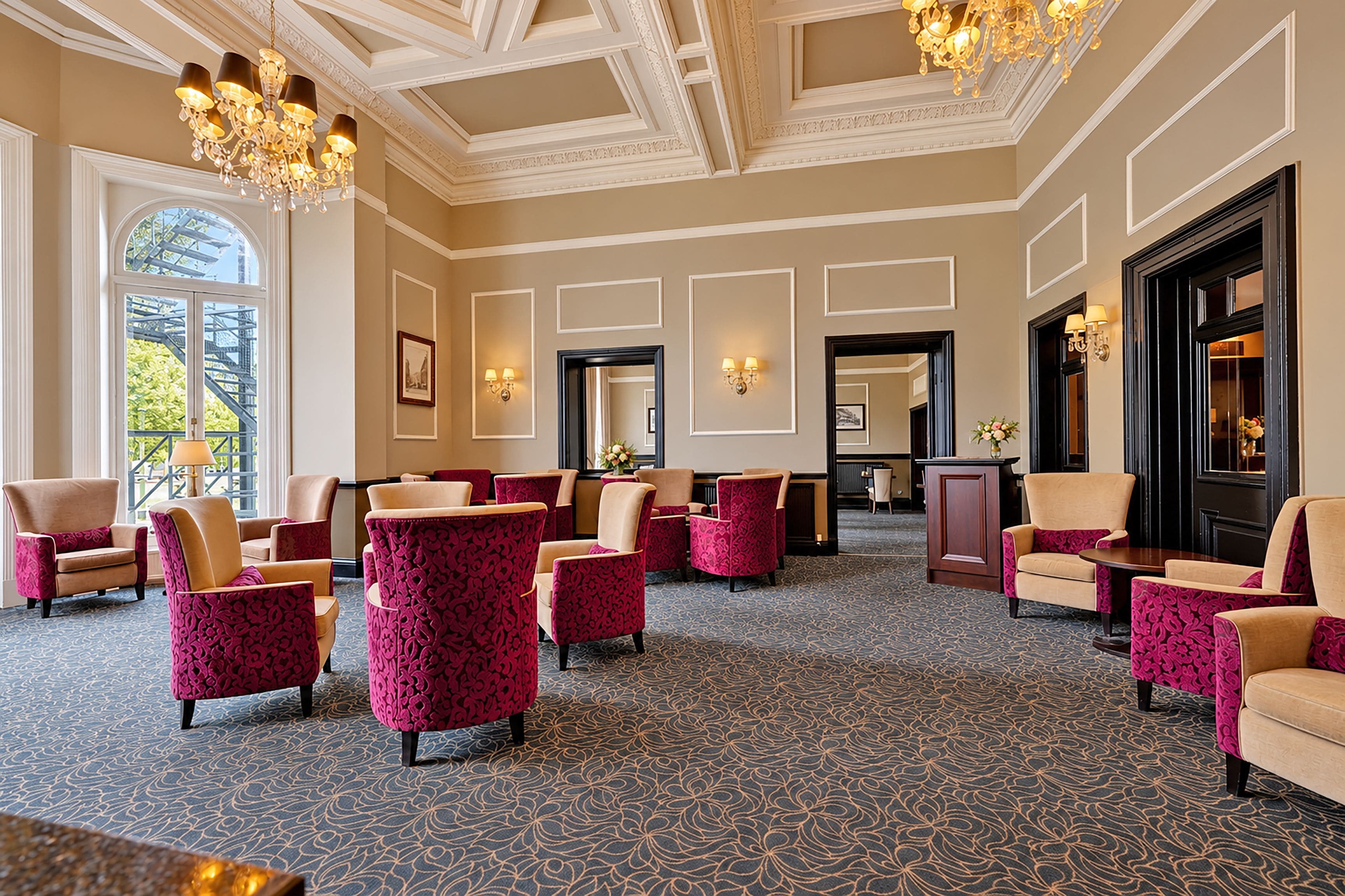 A hotel lobby with patterned carpet, multiple seating areas, chandeliers, and framed artwork on the walls.