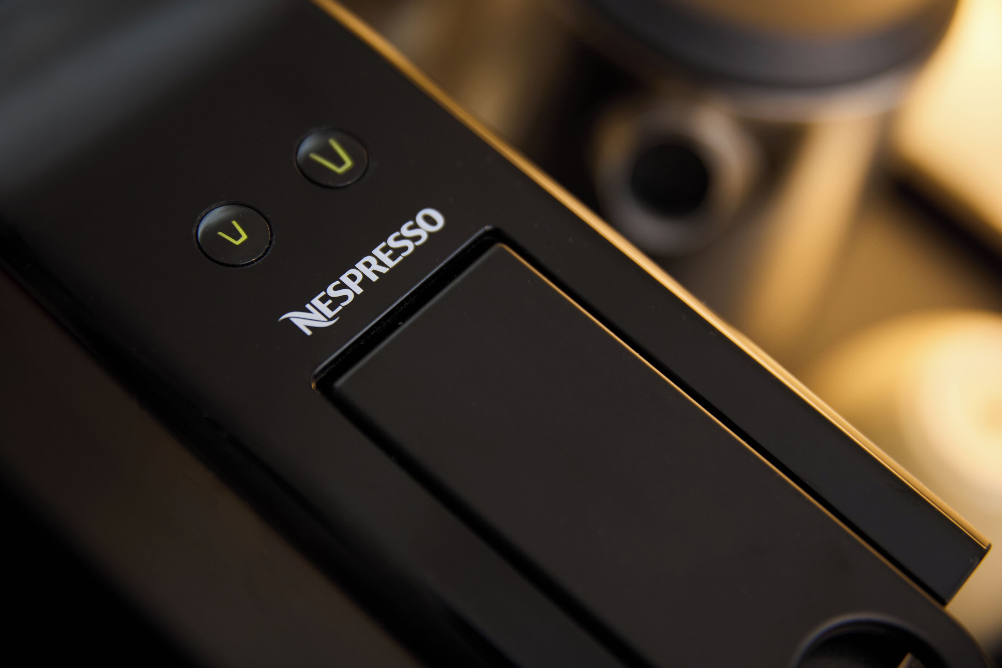A close-up of a black electronic device with the brand name "NESPRESSO" and two illuminated buttons.