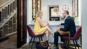 A reception area with a reception desk, a staircase, and a clock on the wall. - Blandford Hotel (London)