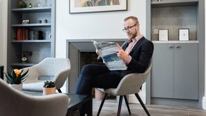 A man reading a newspaper in a modern living room with a fireplace, bookshelves, and decorative items. - Blandford Hotel (London)